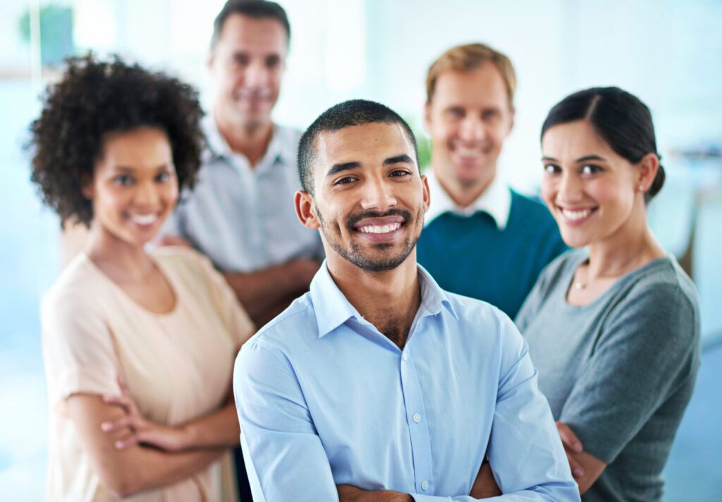 A group of five diverse people from Cook County Careers smiles confidently, arms crossed, with a focus on a man in the front wearing a light blue shirt. The softly blurred background hints at a casual office setting, embodying the spirit of teamwork and opportunity.